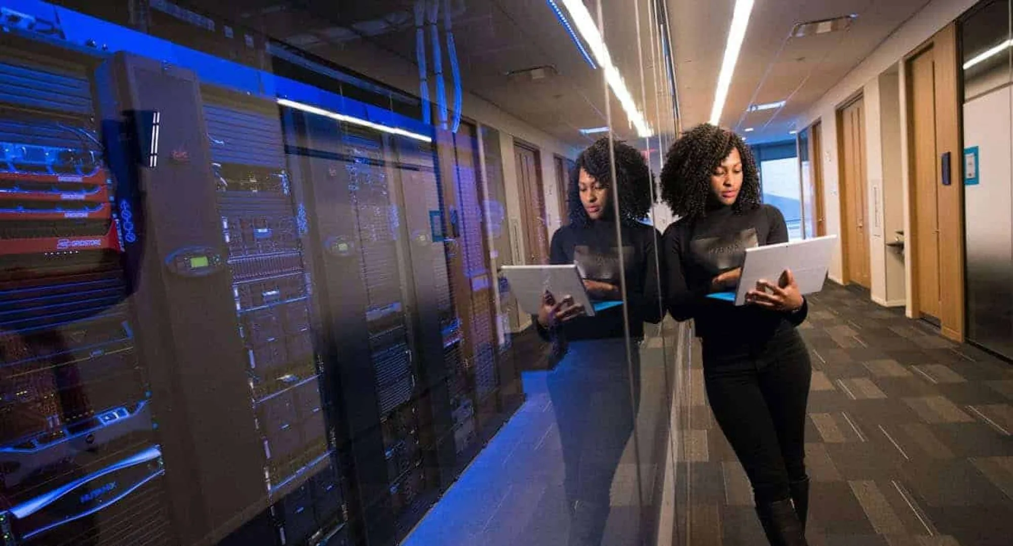 AI Office Developers; women working on tablets in data center; tech team collaborating; modern IT office; cloud computing and server management. Female developers working with tablets in a high-tech data center corridor.